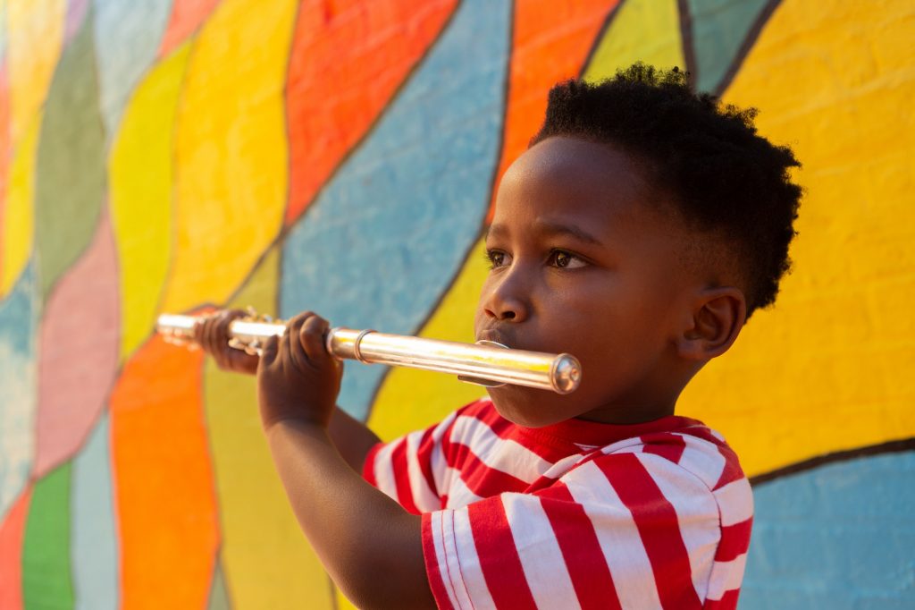 Side view of innocent African-American schoolboy playing flute instrument in the school playground