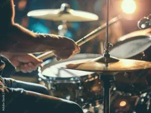 A close-up of a person's hands playing a drum set with drumsticks, focused on the cymbals and snare drum, with bright stage lighting in the background—capturing the energy and precision taught at East Orlando School of Music.