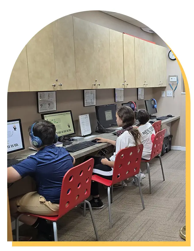 Three children wearing headphones sit at a row of computers, each using a keyboard piano learning program. They are seated on red chairs in a classroom, typical of music lessons Westchase students might enjoy.