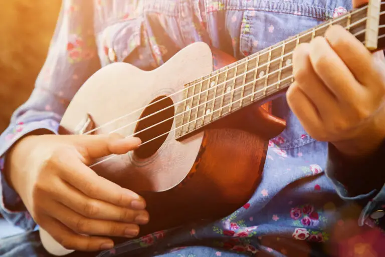 A person wearing a floral blue shirt strums a small wooden ukulele, with sunlight shining on their hands and the instrument—capturing the joyful spirit inspired by Music Lessons in East Orlando.