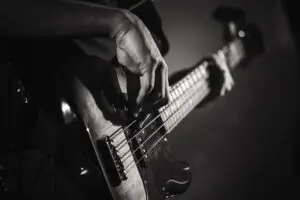 A close-up black and white photo of a person's hand playing an electric bass guitar, focusing on the fingers plucking the strings and the instrument’s body—capturing the dedication and skill honed through Music Lessons in East Orlando.
