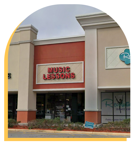A storefront in a strip mall with a red and white sign that reads “Music Lessons” above the entrance; windows display posters for Step Up music lessons, and there is a neighboring dance studio visible on the right.