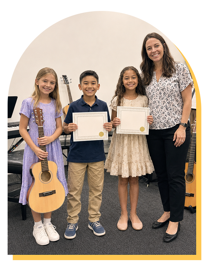 Three smiling children stand with certificates and a guitar, next to an adult woman in a music school setting. Musical instruments in the background suggest they’ve just finished music lessons Citrus Park or an award event in music lessons Tampa.