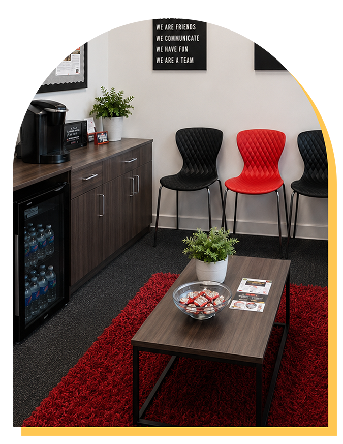 A modern waiting room at Step Up music lessons in Citrus Park features a coffee station, mini fridge, three black chairs, one red chair, snacks and plants on the table, and a red rug. Wall signs inspire teamwork and communication.